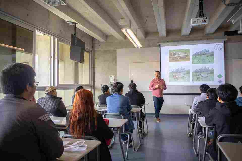 Profesor dictando una clase interactiva con proyectores ante un grupo de estudiantes, reflejando los estándares de calidad educativa en Perú